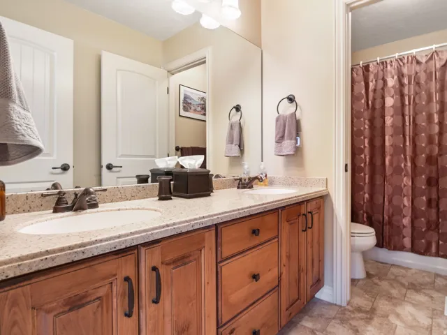Hall bathroom. Dual vanity with integrated sinks, wood-finish cabinetry, and solid surface countertops.