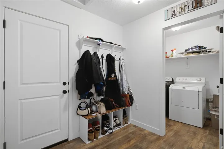 Mudroom entry with wood-finish flooring, white paneled door, built-in coat rack and shelving, and recessed lighting