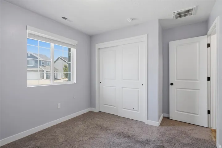 Carpeted room featuring a double-pane window with grids, white trim, sliding closet doors, and light gray walls