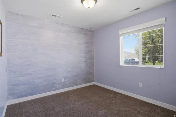 Carpeted room with a textured accent wall and a window featuring white blinds