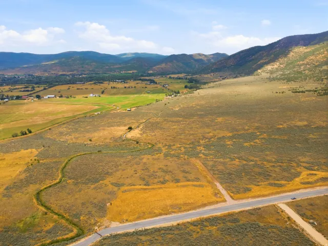 Expansive land parcel featuring natural terrain, paved road frontage, and distant mountain backdrops
