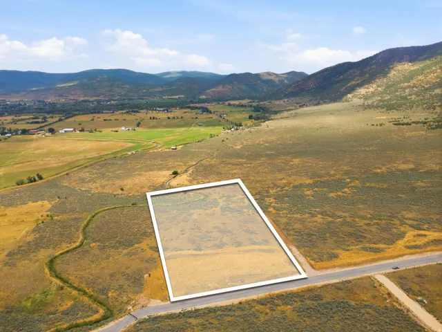 Rectangular land plot with mountain backdrop, surrounded by expansive natural terrain, featuring a paved road frontage and a natural water channel