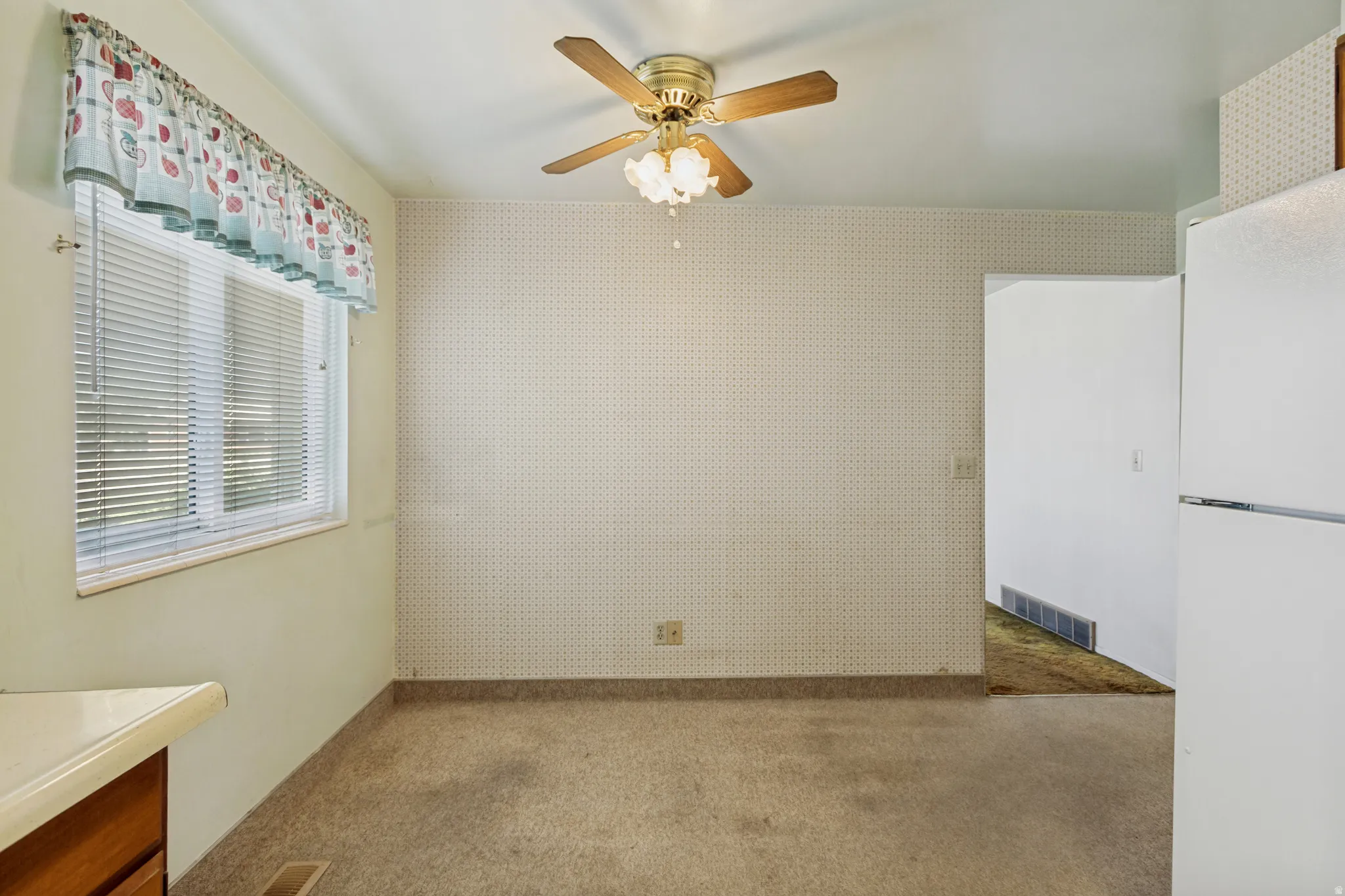Ceiling fan with light fixture, window with horizontal blinds, carpeted flooring, and light-colored countertops