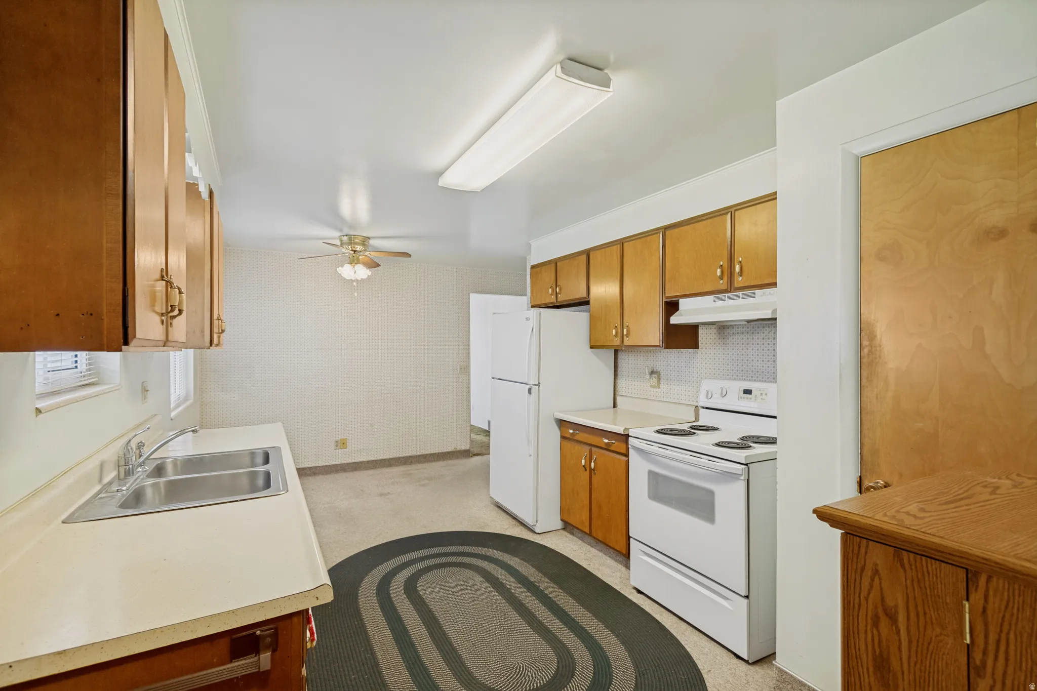 Kitchen featuring wood-finish cabinetry, a double basin stainless steel sink, white appliances, and a ceiling fan