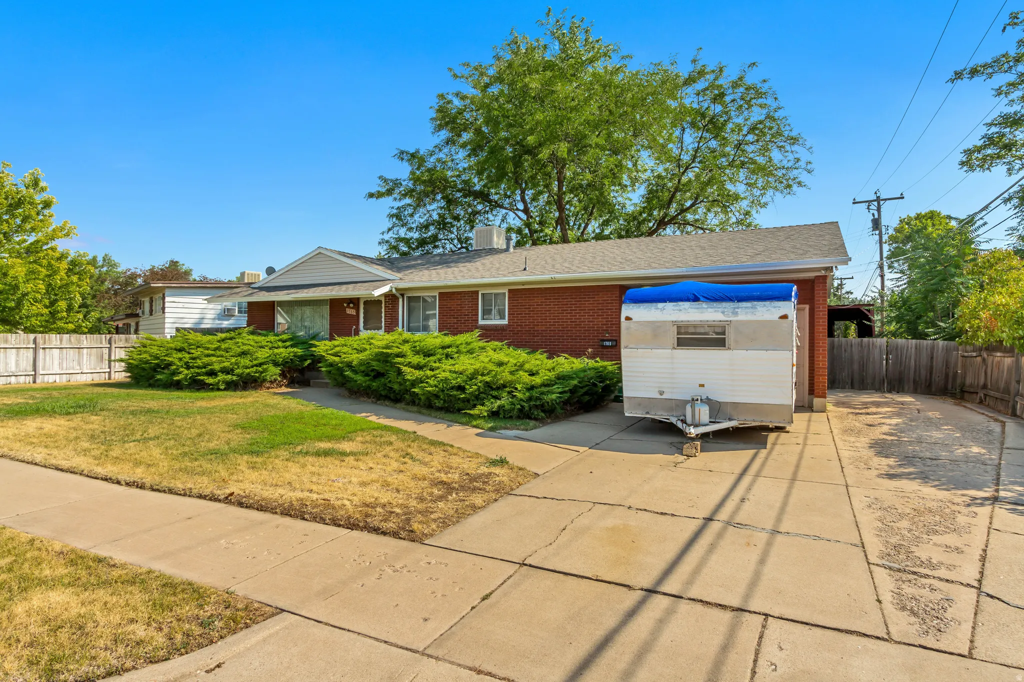 Brick exterior with white trim, front lawn, mature shrubbery, concrete driveway, and wood fencing