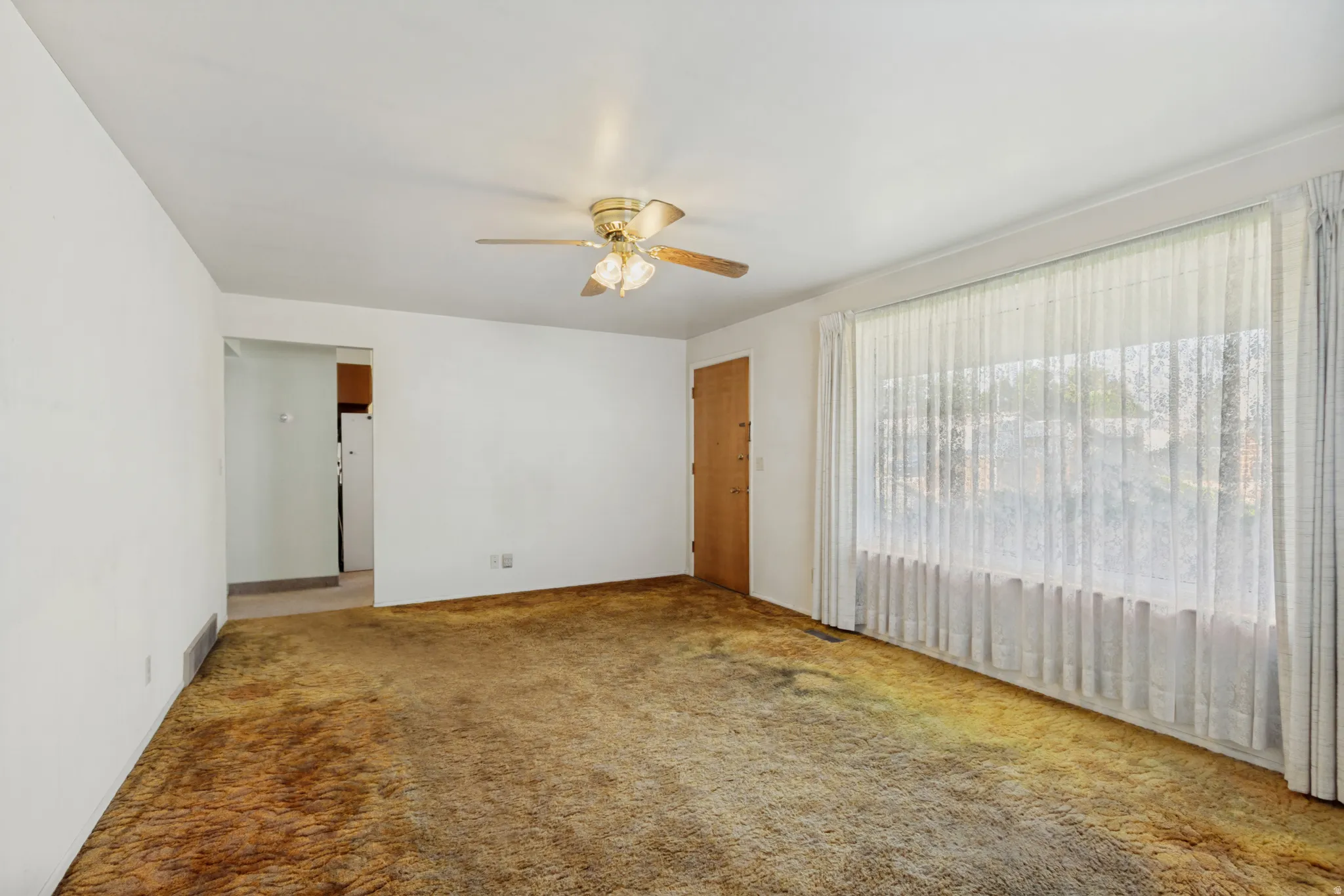 Expansive living area featuring a large picture window, ceiling fan, and carpeted flooring