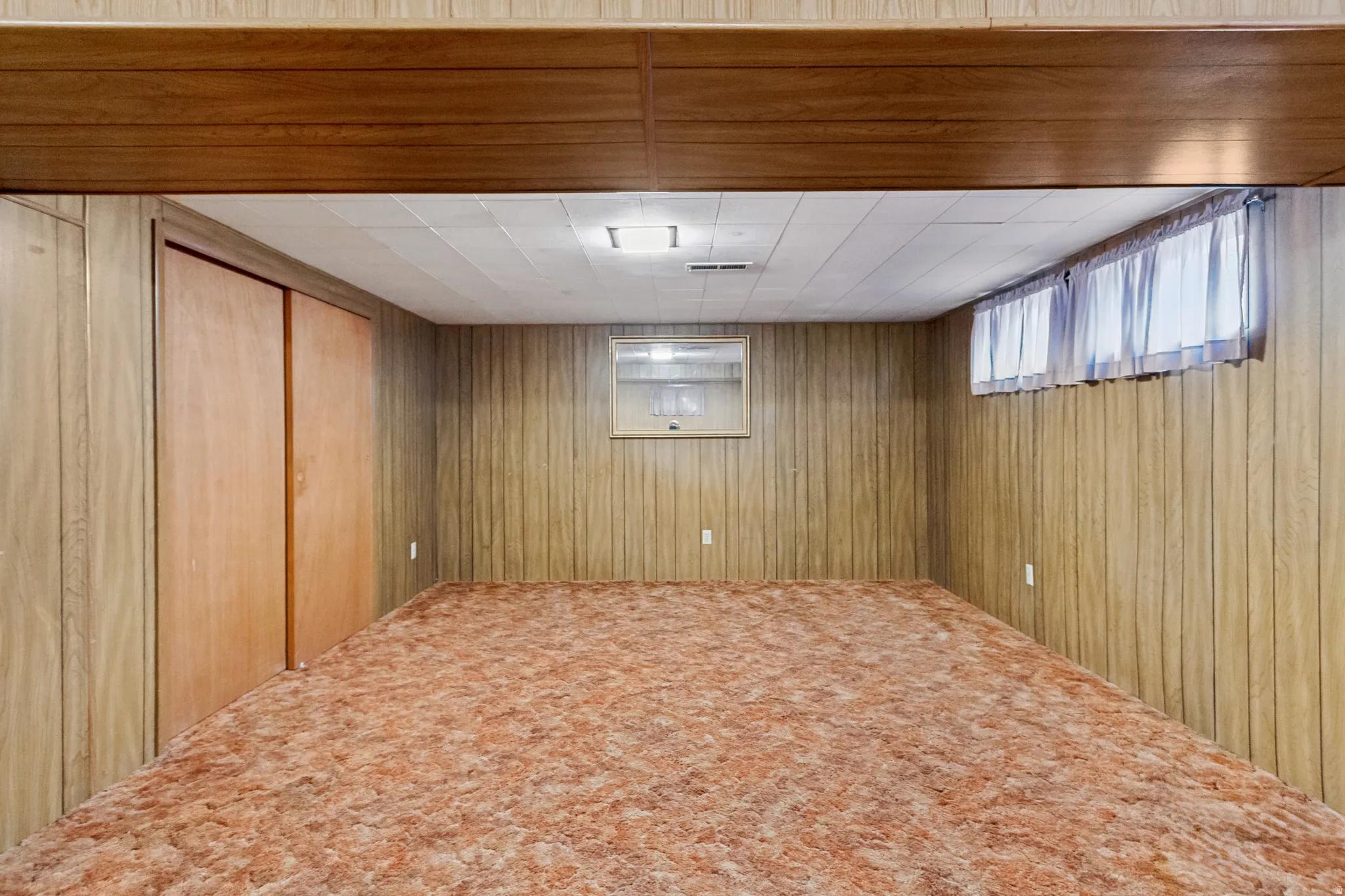 Finished room featuring wood-panel walls, carpet flooring, and a drop ceiling with recessed lighting