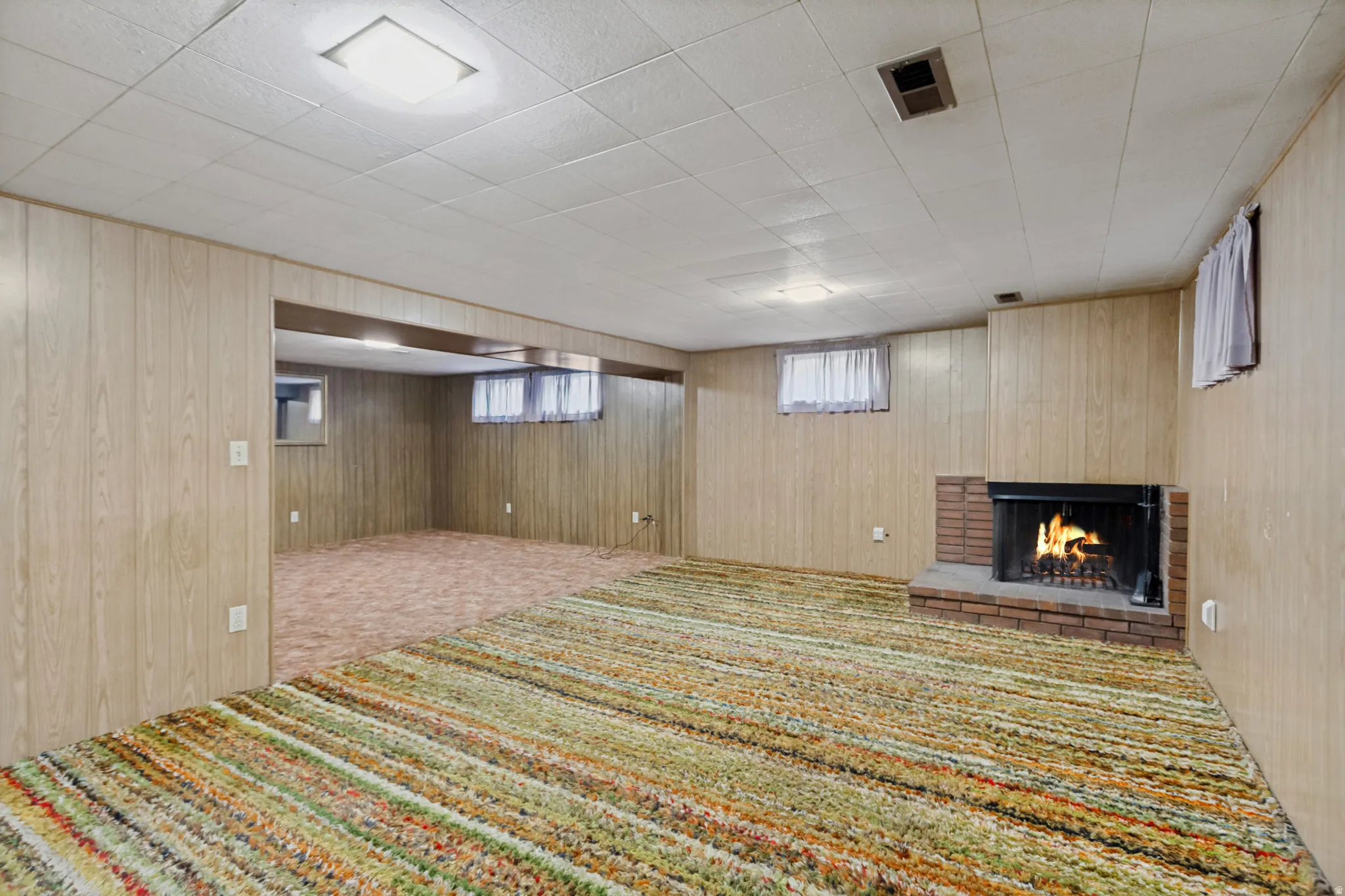 Brick fireplace with hearth, wood-panel walls, and recessed lighting