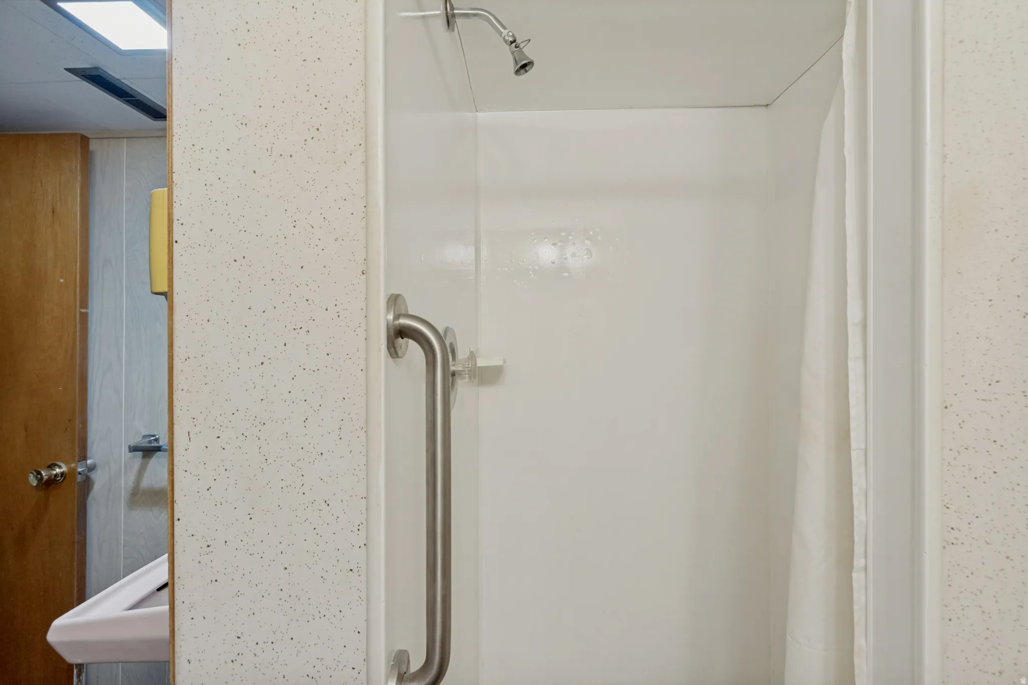 Stand-up shower with a wall-mounted showerhead, brushed nickel grab bar, and white surround