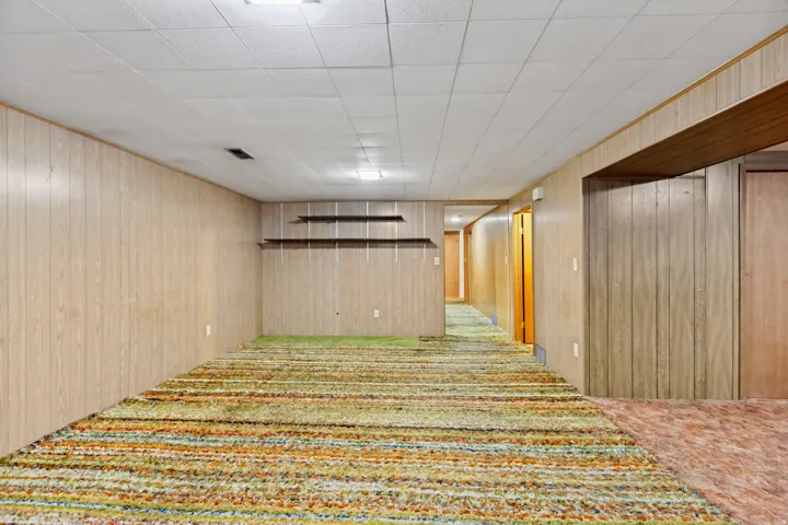 Recessed lighting illuminates the space, featuring wood-finish paneling, built-in shelving, and varied carpeting