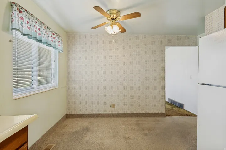 Ceiling fan with light fixture, window with horizontal blinds, carpeted flooring, and light-colored countertops