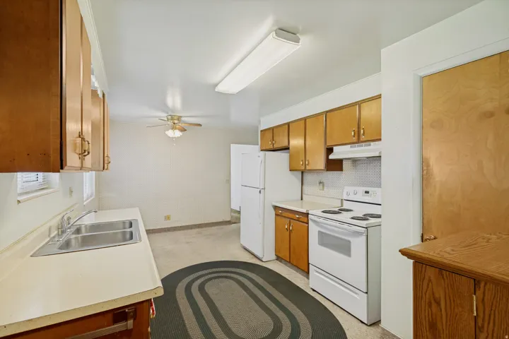 Kitchen featuring wood-finish cabinetry, a double basin stainless steel sink, white appliances, and a ceiling fan