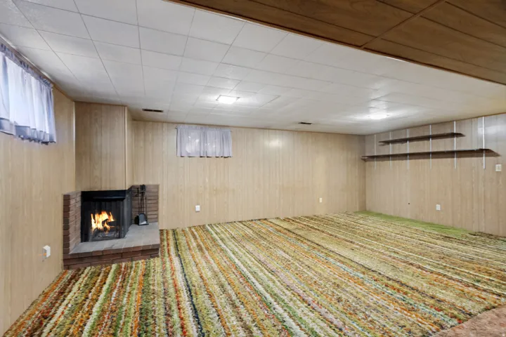 Brick fireplace with hearth, wood paneling, acoustic tile ceiling, recessed lighting, and built-in shelving