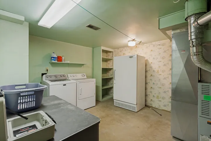 Laundry area featuring a washer and dryer, built-in shelving, concrete flooring, and a utility sink