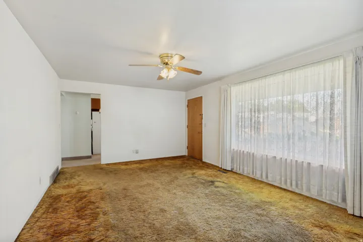 Expansive living area featuring a large picture window, ceiling fan, and carpeted flooring
