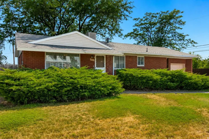 Charming brick ranch home featuring a gabled roofline, front-facing covered entry, and expansive manicured lawn framed by mature landscaping and established trees