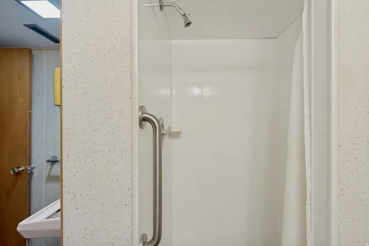 Stand-up shower with a wall-mounted showerhead, brushed nickel grab bar, and white surround