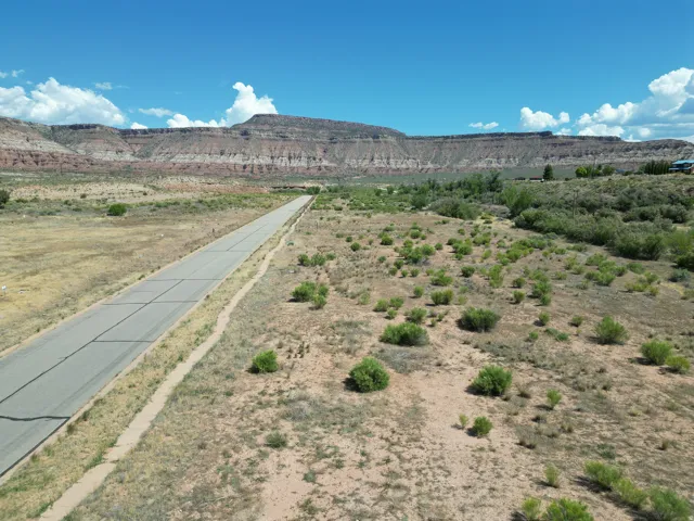 Expansive undeveloped land featuring a paved road, natural desert foliage, and distant mountainous terrain