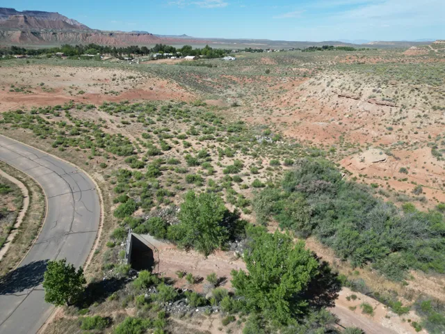 Curved paved road bordering natural desert landscaping with sparse green vegetation and distant natural rock formations