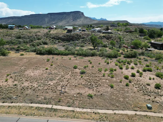 Expansive undeveloped land featuring natural desert flora, a partial sidewalk border, and distant mountain backdrops
