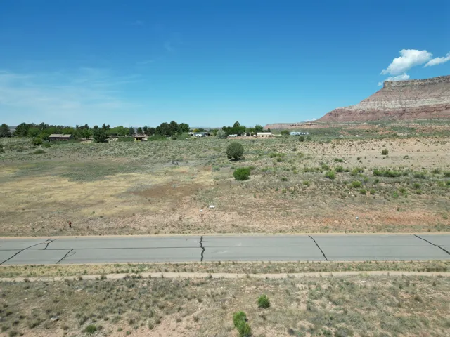 Expansive undeveloped land featuring a paved road, arid vegetation, and a distant mesa backdrop
