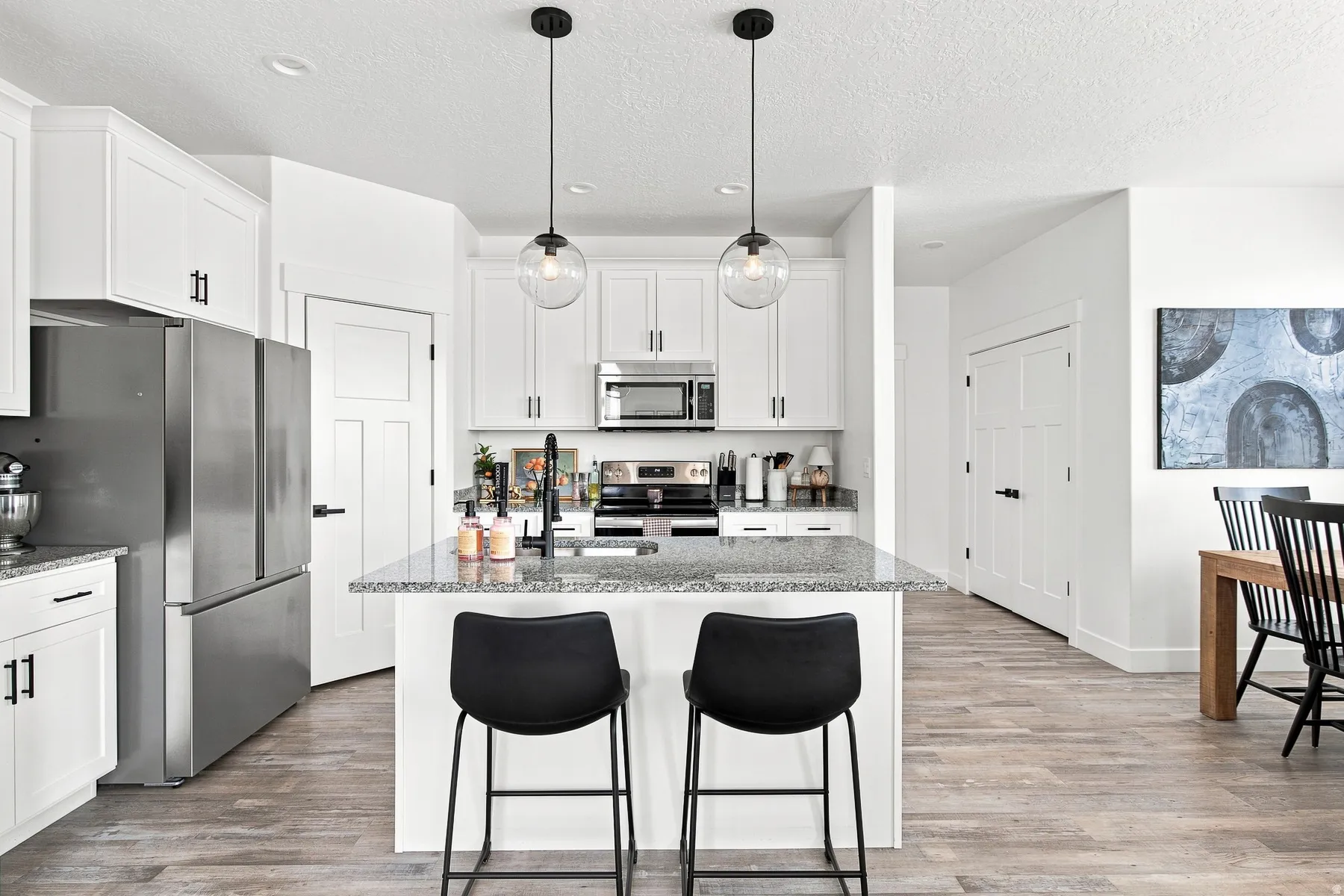 Kitchen featuring white cabinetry, stainless steel appliances, a center island with a stone-finish countertop, and wood-finish flooring