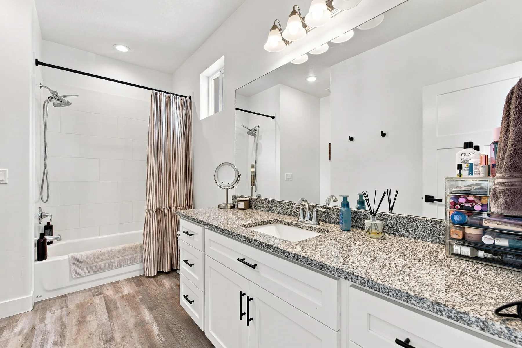 Vanity with granite-style countertop, integrated sink, and white cabinetry with black hardware