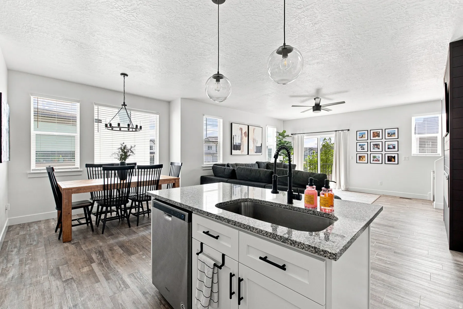 Open-concept living space featuring wood-finish flooring, a kitchen island with granite countertops, and a stainless steel dishwasher