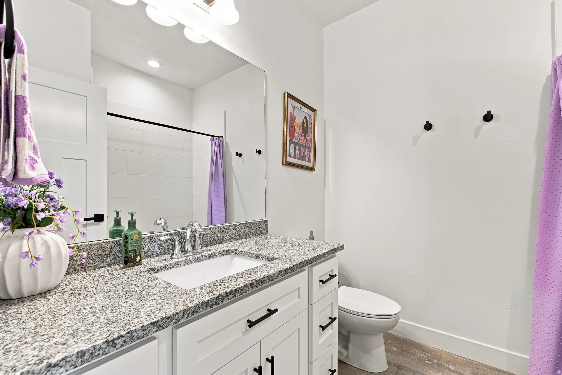 White shaker-style vanity with dark hardware, granite countertop, undermount sink, and chrome faucet