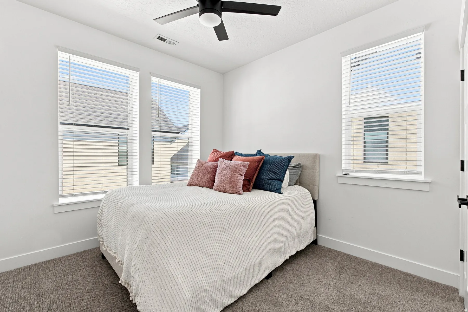 Recessed ceiling with an attached black ceiling fan, white walls, multiple windows with blinds, and carpeted flooring