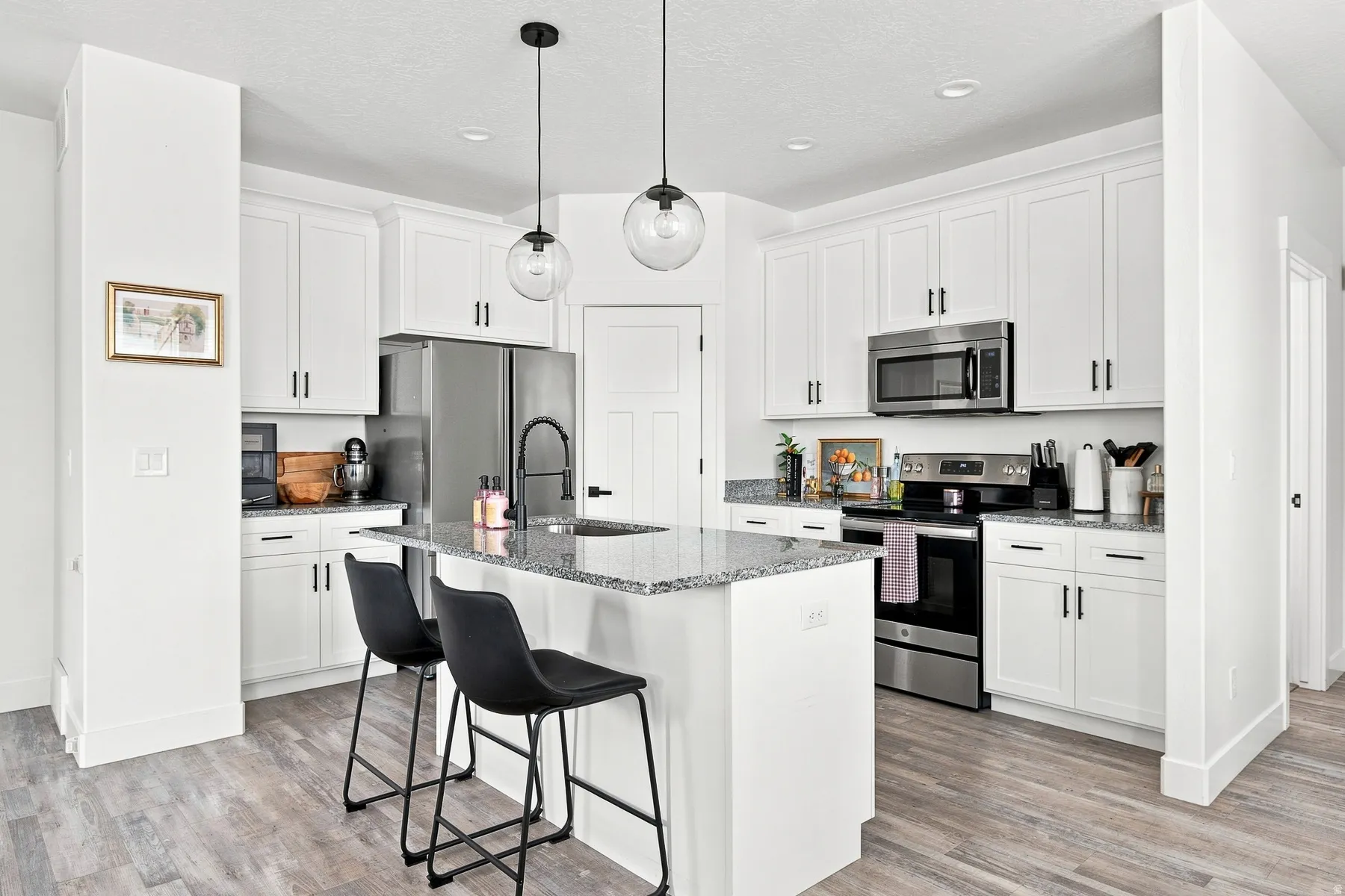 Kitchen featuring white cabinetry, stainless steel appliances, granite countertops, and wood-finish flooring