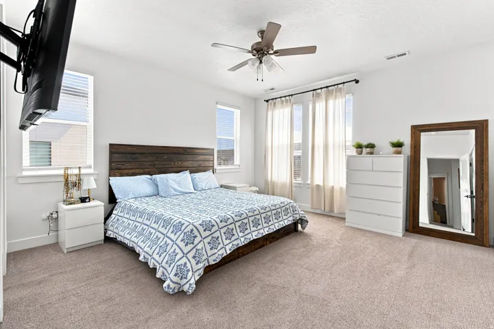 Plush carpet flooring, multiple windows with blinds, a ceiling fan, and a wood-paneled headboard