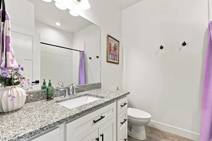 White shaker-style vanity with dark hardware, granite countertop, undermount sink, and chrome faucet