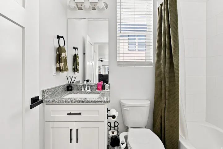 White vanity with shaker-style cabinetry, granite-finish countertop, and undermount sink