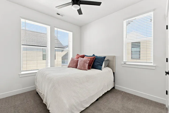 Recessed ceiling with an attached black ceiling fan, white walls, multiple windows with blinds, and carpeted flooring