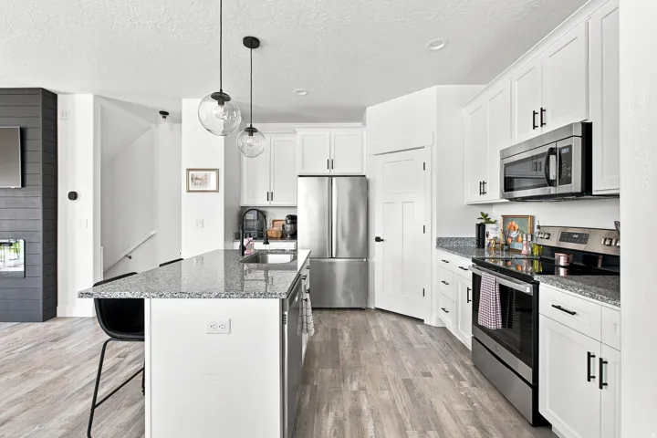 Modern kitchen featuring white cabinetry, stainless steel appliances, a center island with bar seating, pendant lighting, and wood-finish flooring