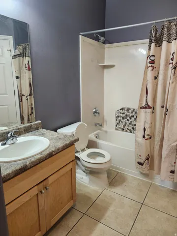 Full bathroom featuring a single vanity with wood-finish cabinetry, a toilet, and a combined tub and shower with a built-in shelf