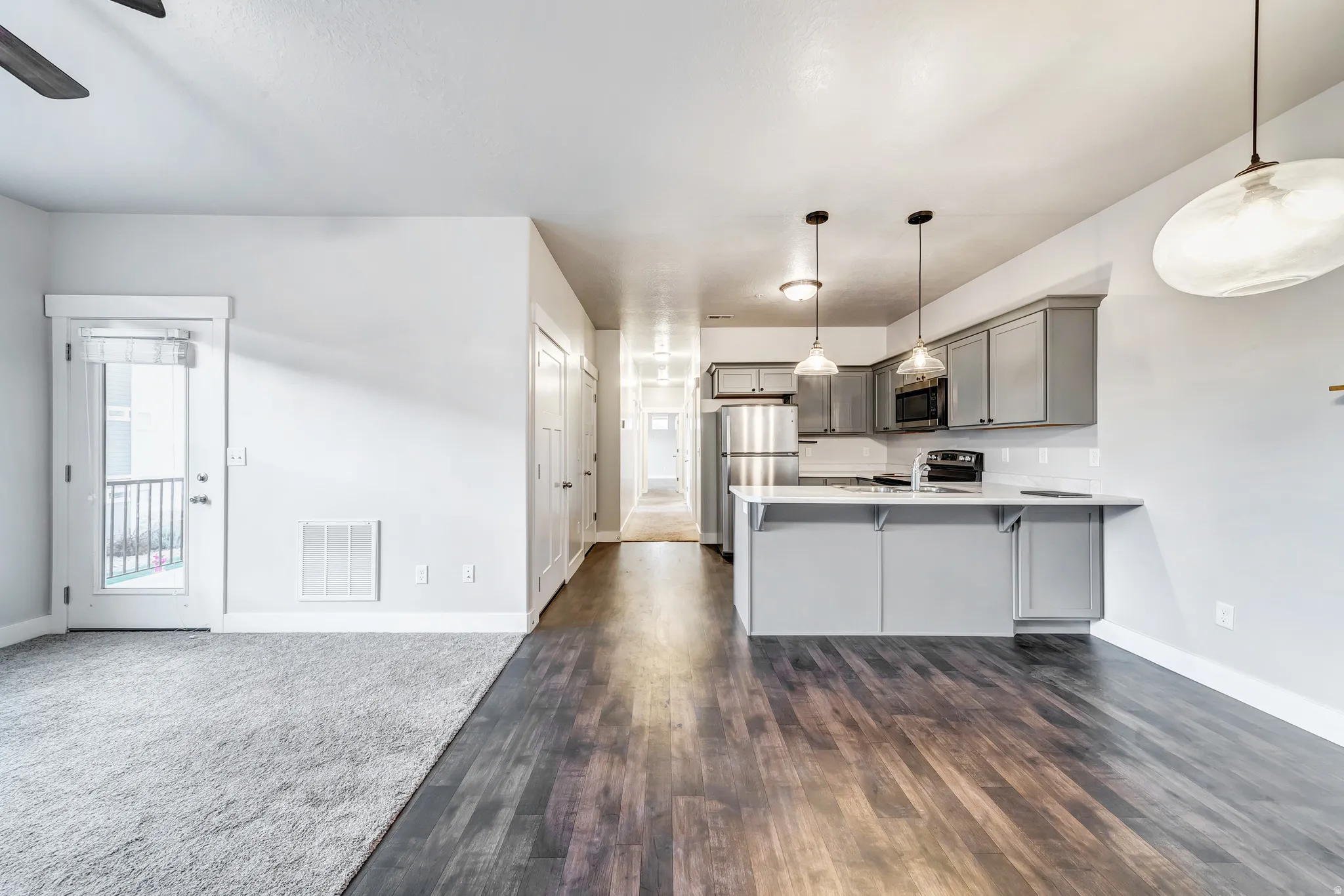 Wood-finish flooring, light grey cabinetry, stainless steel appliances, white countertops, and a full-light exterior door