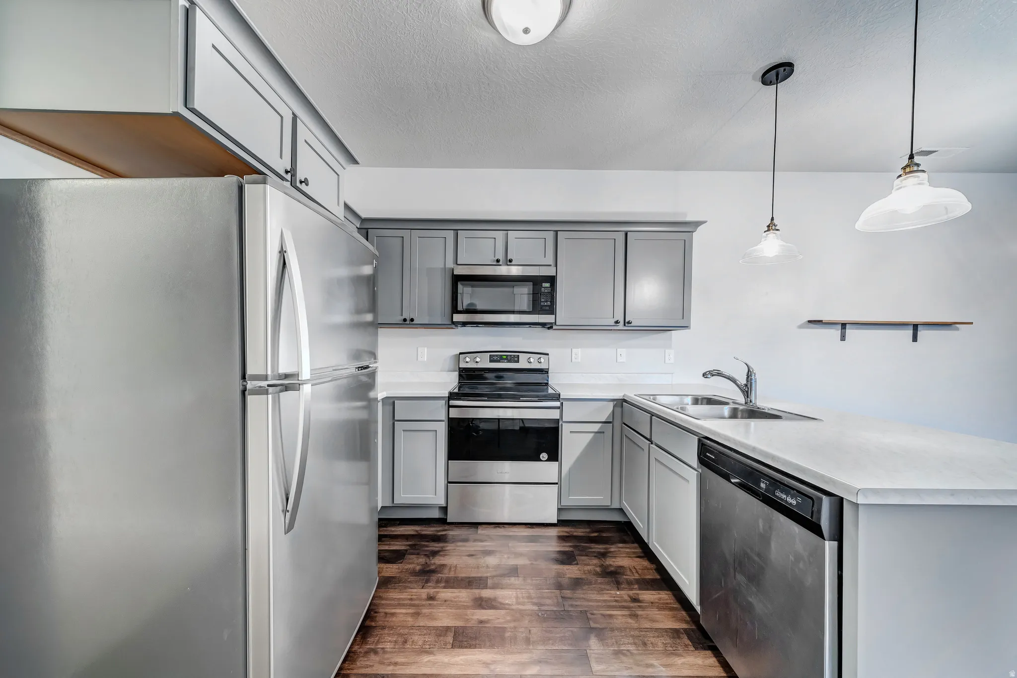 Kitchen featuring stainless steel appliances, grey cabinetry, light countertops, a dual-basin sink, and wood-finish flooring