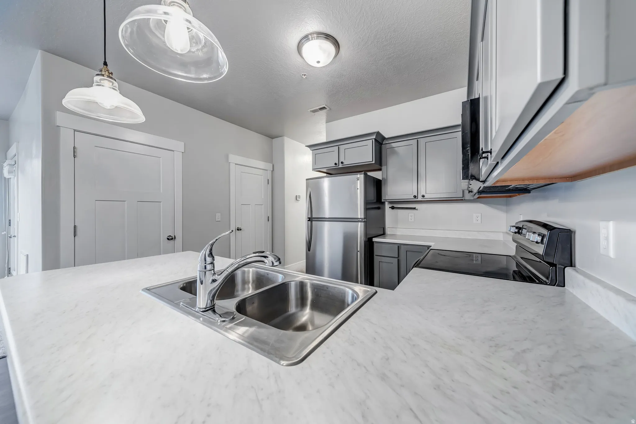 Modern kitchen featuring a stainless steel double-basin sink with chrome faucet, white quartz countertops, white cabinetry, stainless steel appliances including a refrigerator and range, pendant lighting, and recessed ceiling fixtures
