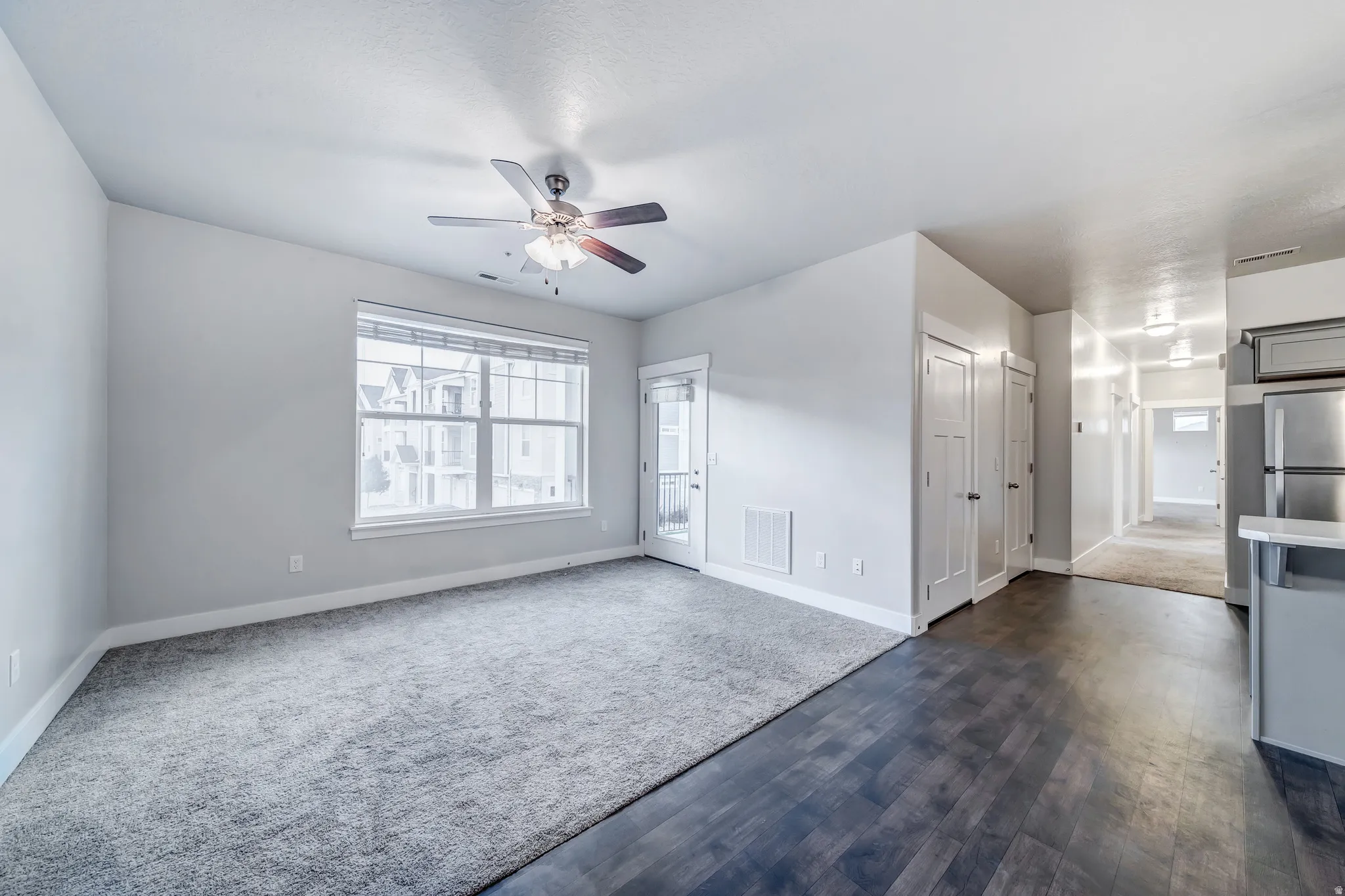 Bright corner bedroom with dual windows providing natural light, ceiling fan with integrated lighting fixture, carpeted flooring, and direct access to hallway with adjacent closet storage and en-suite bathroom entry