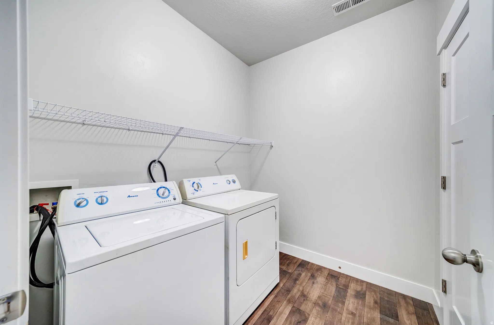 Laundry area featuring wood-finish flooring, white walls, and a wire shelf