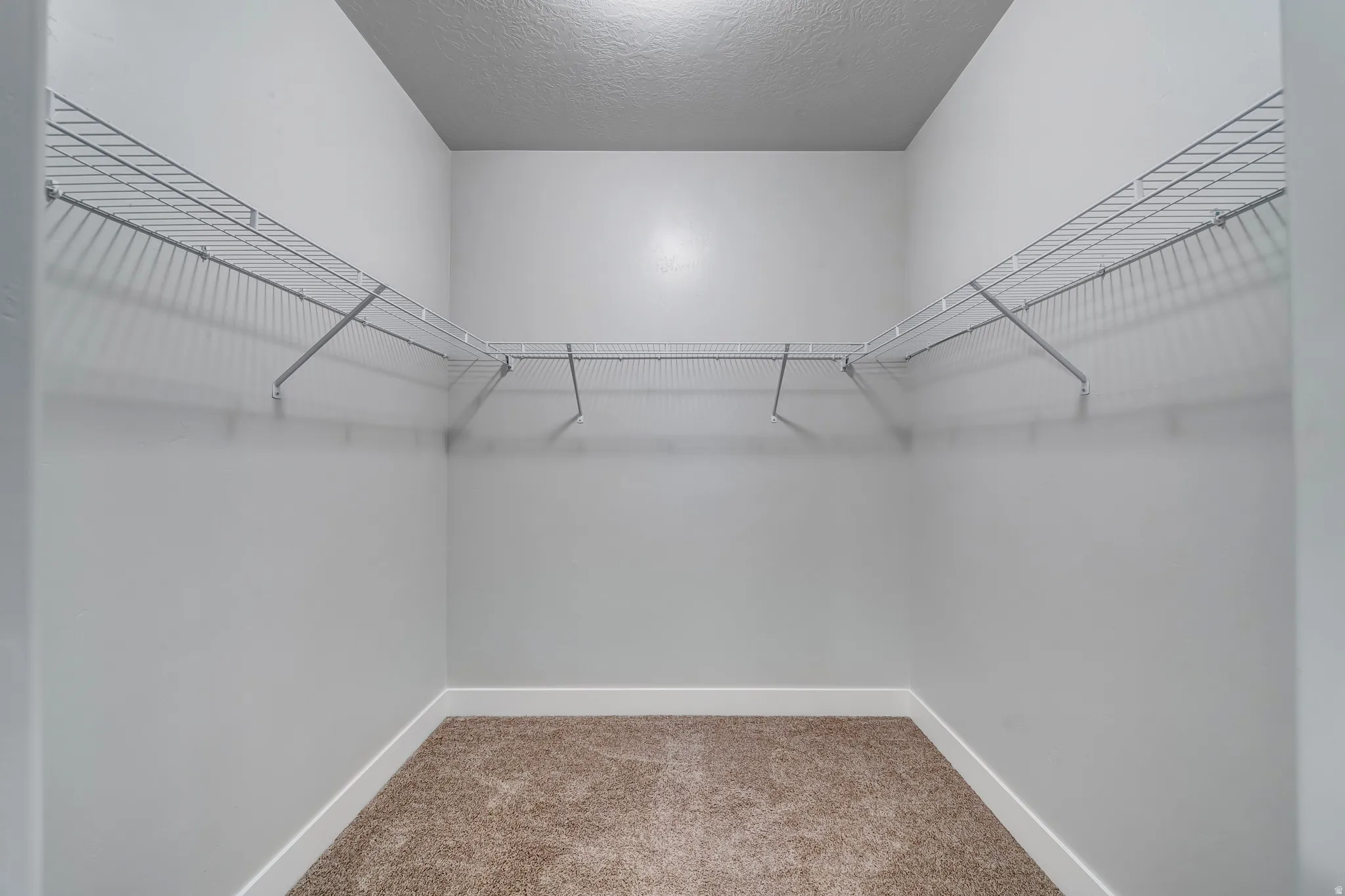 Integrated wire shelving, wire hanging rods, neutral carpet flooring, and clean white walls