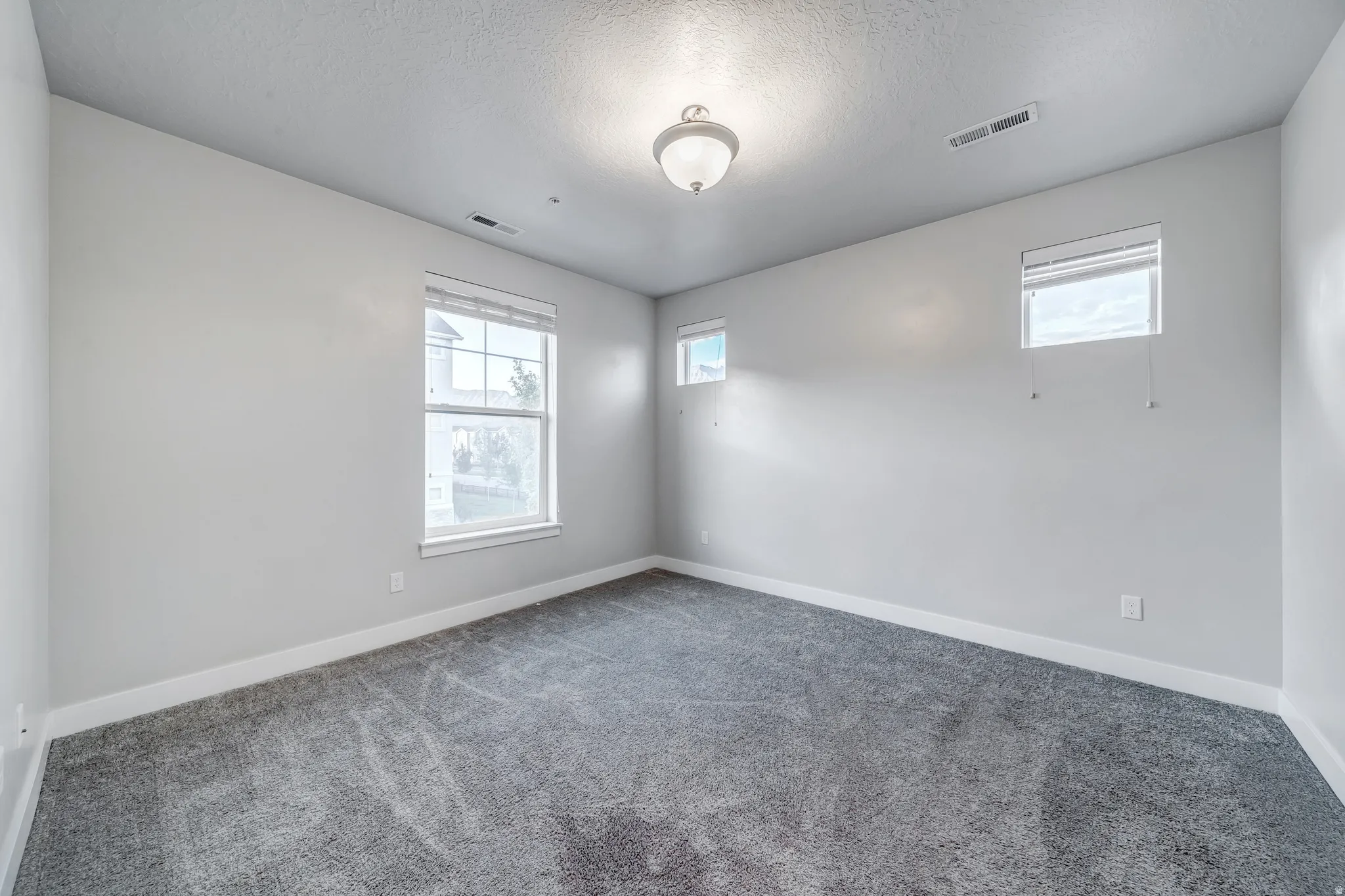 Light gray wall paint, gray carpeting, multiple windows, and a semi-flush mount ceiling light