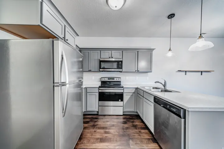 Kitchen featuring stainless steel appliances, grey cabinetry, light countertops, a dual-basin sink, and wood-finish flooring