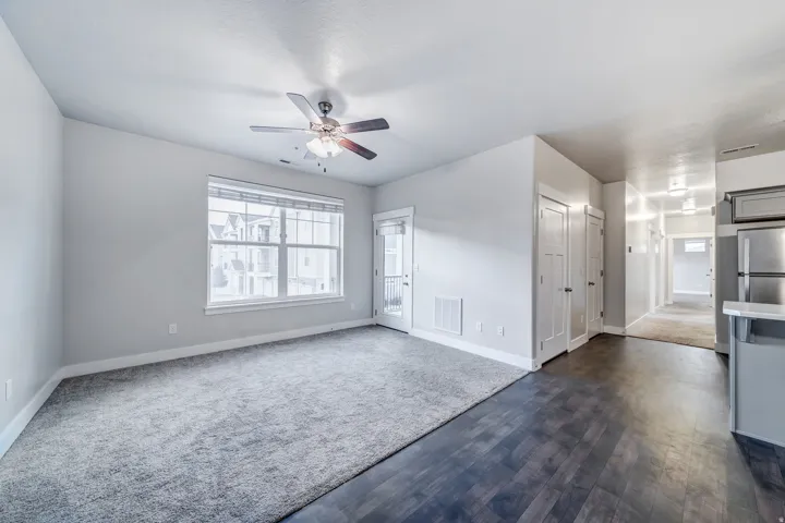 Bright corner bedroom with dual windows providing natural light, ceiling fan with integrated lighting fixture, carpeted flooring, and direct access to hallway with adjacent closet storage and en-suite bathroom entry