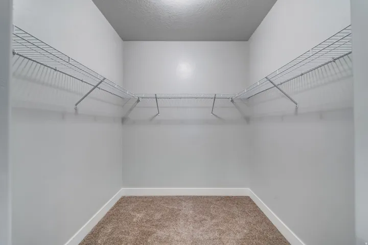 Integrated wire shelving, wire hanging rods, neutral carpet flooring, and clean white walls