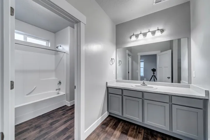 Bathroom featuring a single vanity with gray cabinetry, a white countertop, and a large mirror with overhead lighting