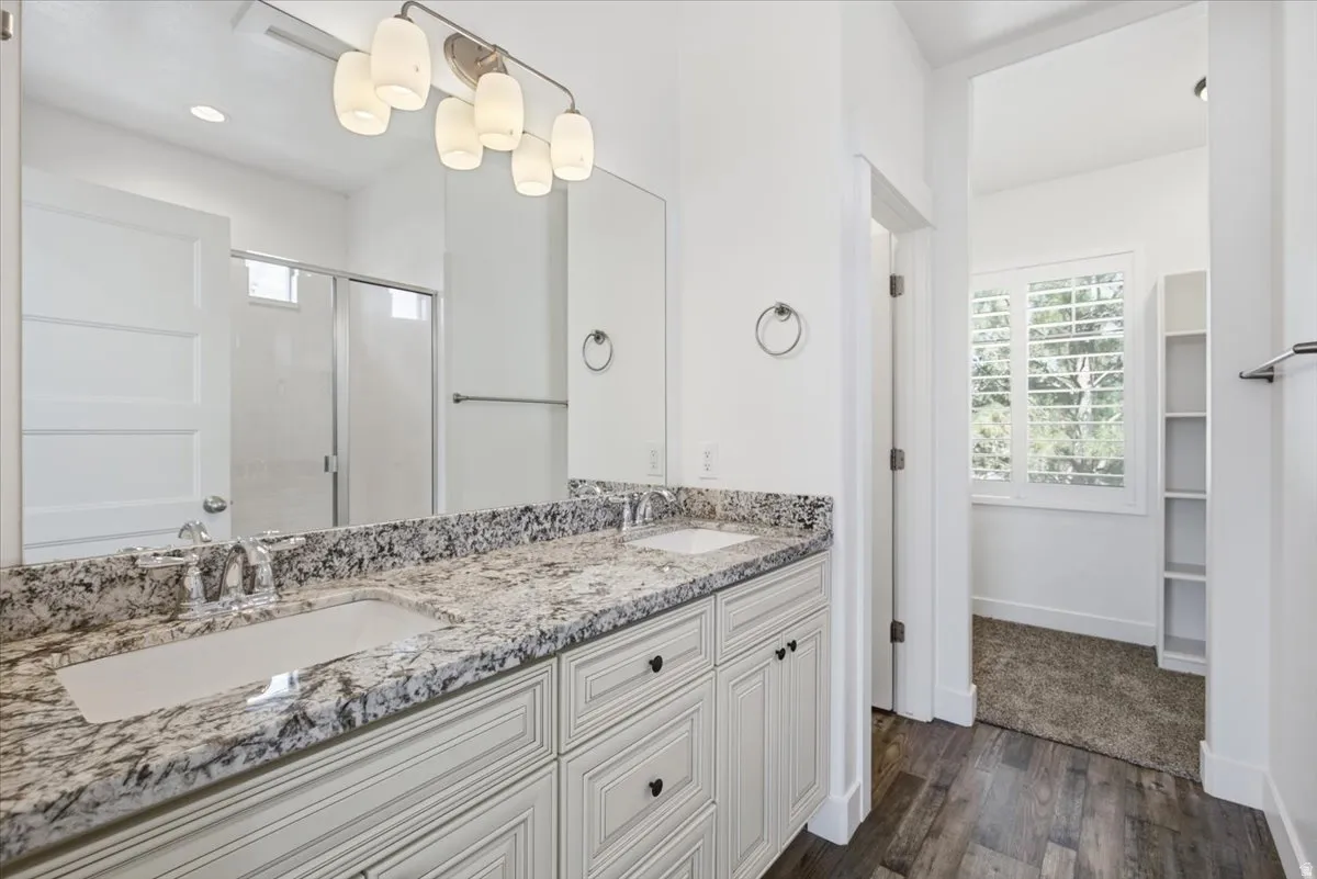 Dual vanity with stone-finish countertop, wood-finish flooring, built-in shelving, and a shower enclosure