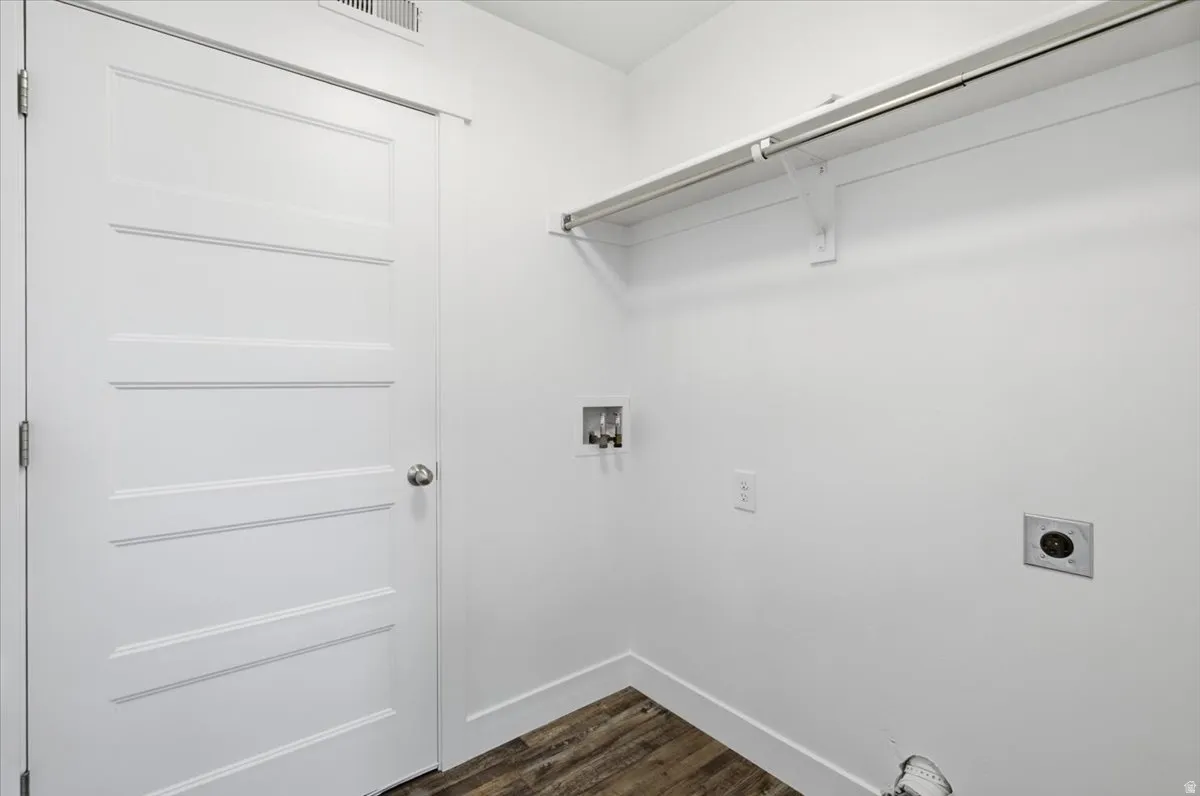 Laundry area featuring wood-finish flooring, white walls, and a built-in shelving unit with hanging rod